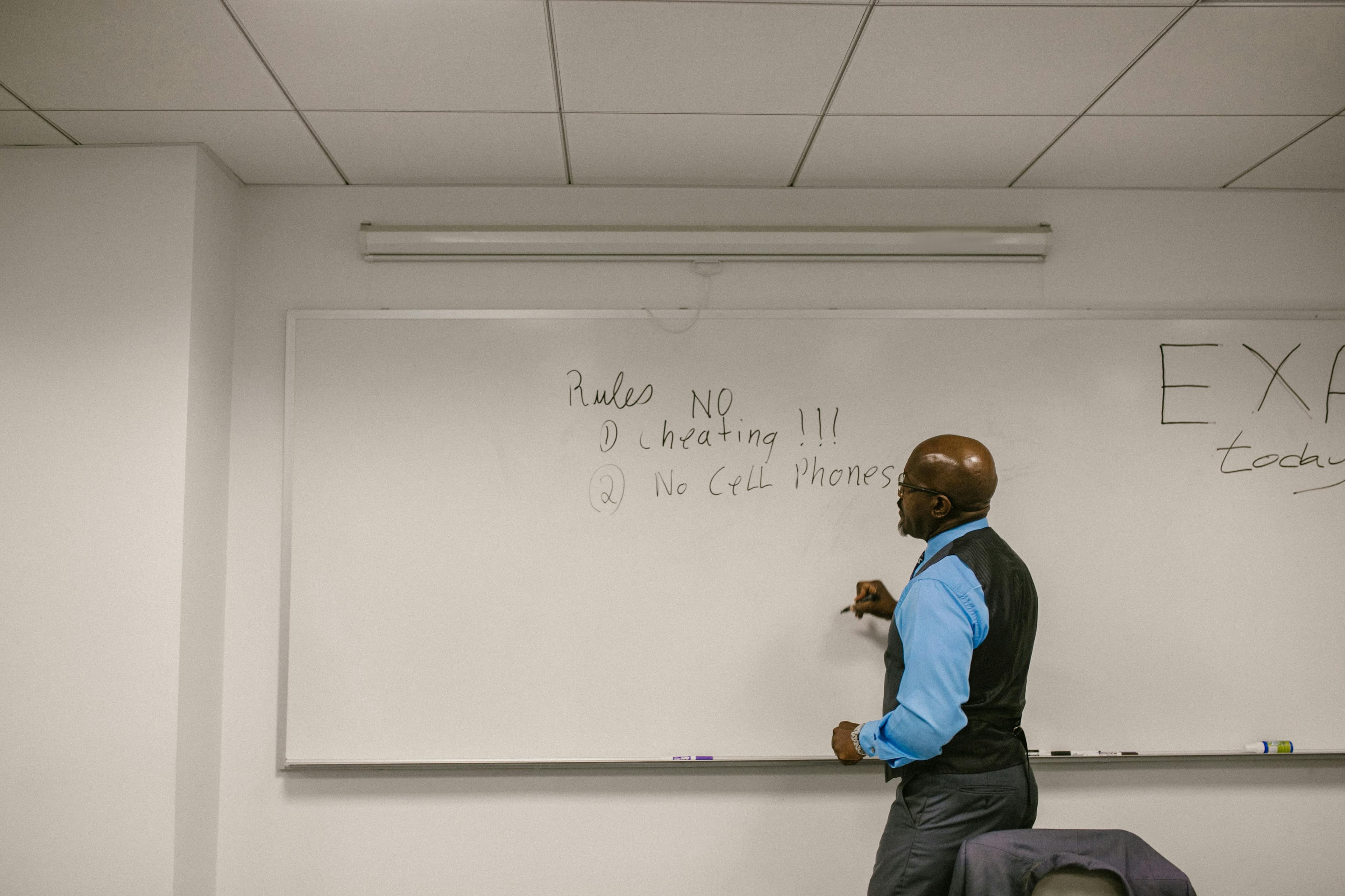 Instructor preparing a classroom whiteboard with exam rules before a test.